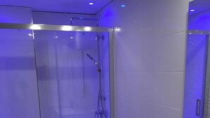 Un baño moderno con ducha envuelta en cristal, inodoro blanco y lavabo blanco con un espejo encima.