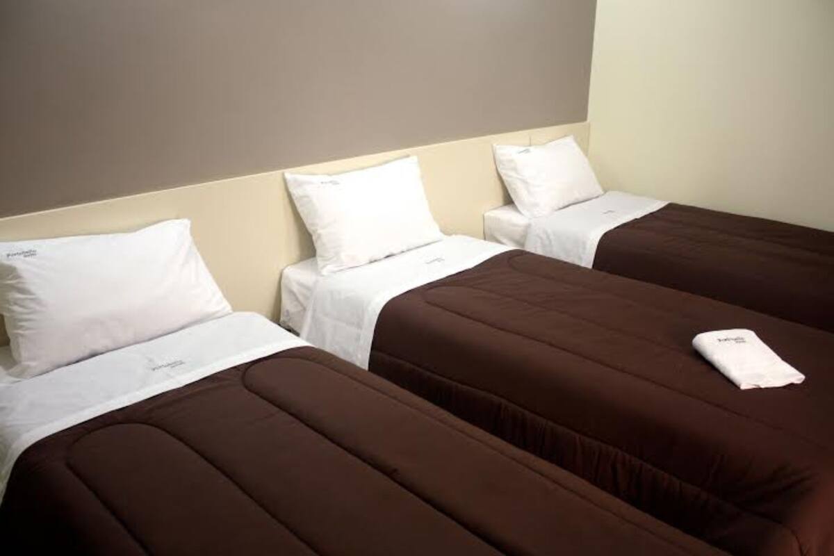 A hotel room with three beds, each with a brown bedspread and white pillows.