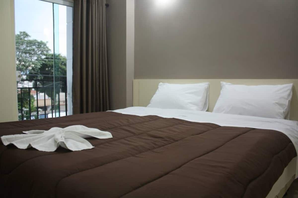 A hotel room with a large bed, a view of the outdoors through a window, and a balcony.