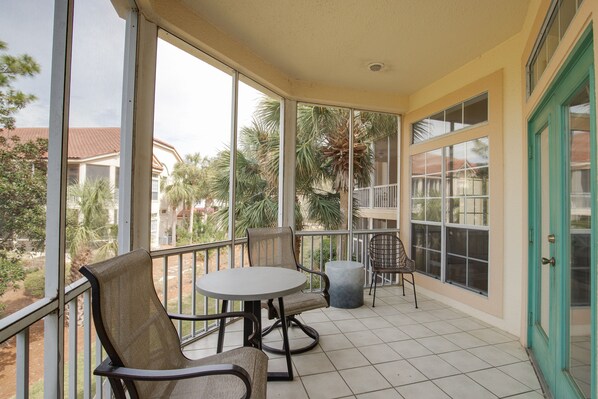 A covered balcony with a table and chairs, large windows, and a view of palm trees and houses.