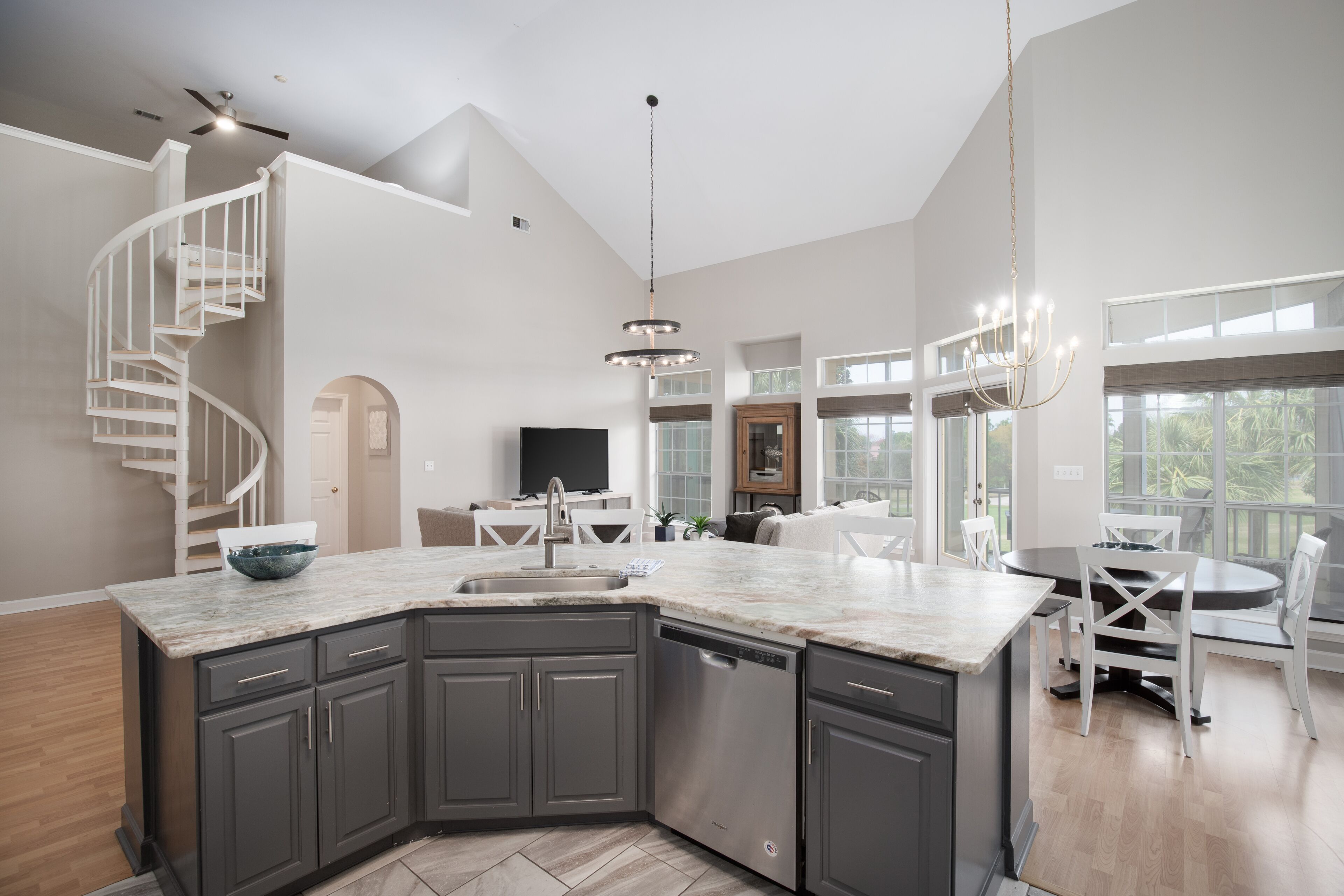 A spacious kitchen with a curved island, dark gray cabinets, and a modern chandelier.