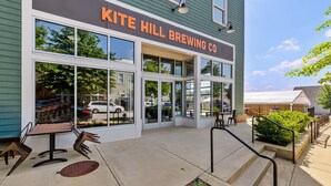The exterior of Kite Hill Brewing Co. with large windows, a patio area with outdoor seating, and a clear sky. - Clemson Lover's Dream Cottage (Clemson)