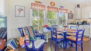 A dining area with blue chairs and a table, a rocking chair, and a window with blinds. - Clemson Lover's Dream Cottage (Clemson)