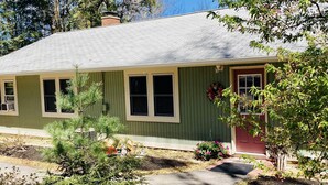 A single-story house with a green exterior, a red door, and a small front yard with a tree and a flower bed. - Convenient, clean and cozy 3 bedroom, 2 bath overlooking idyllic lake whittemore (Spencer)