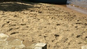 A boat docked at a sandy beach with a stone wall and dock in the foreground. - Convenient, clean and cozy 3 bedroom, 2 bath overlooking idyllic lake whittemore (Spencer)