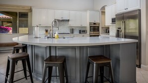 Une cuisine moderne avec des meubles blancs, un grand îlot central doté de tabourets, des appareils en acier inoxydable et un luminaire suspendu.