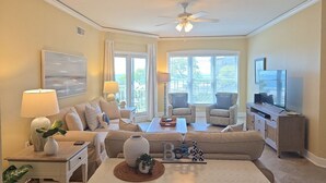 Ein Wohnzimmer mit Sofa, Sesseln, einem Couchtisch, einem Fernseher und einem Deckenventilator.