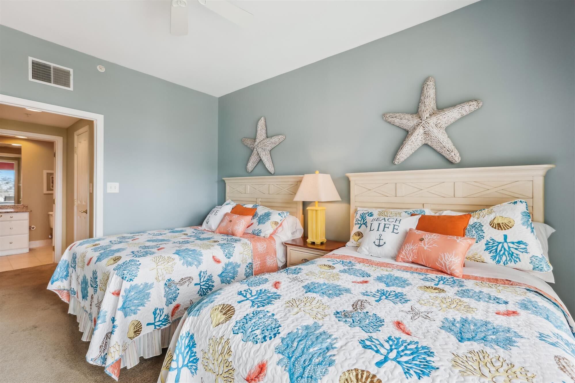 Quarto com duas camas, decoração de parede em formato de estrela-do-mar e mesa de cabeceira com abajur.