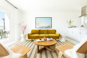 A modern living room with a yellow sofa, a round coffee table, and a view of a white building through a large window.
