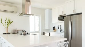 Eine moderne Küche mit weißen Schränken, einem Edelstahl-Kühlschrank, einer Mikrowelle und einer großen Kochinsel mit Sitzgelegenheiten.
