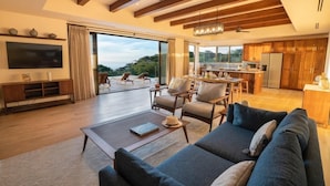 A spacious living area with a sofa, coffee table, and a TV. There is a large window offering a view of the outdoors. - Rancho Santana (Tola)