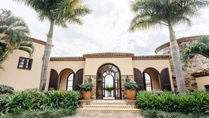 A building with a central arched entrance, flanked by palm trees and potted plants. - Rancho Santana (Tola)