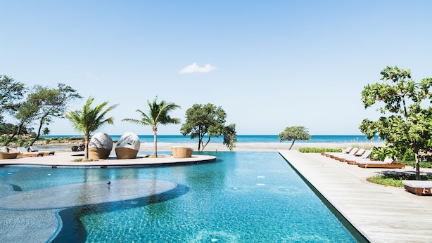 A clear blue pool with a curved edge, surrounded by lounge chairs and palm trees, leading to a beach. - Rancho Santana (Tola)