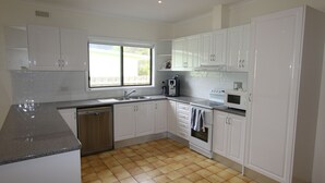 A modern kitchen with white cabinets, a dishwasher, an oven, a microwave, and a window providing natural light. - Silvanas Retreat (COWES)