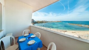 A balcony with a table set for four, overlooking a coastal area with a clear view of the sea and a rocky shoreline. - Amazing apartment in Porto Torres with WiFi (Porto Torres)