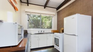 A compact kitchen with white appliances, a window with a view of trees, and a brick wall. - Foreshore Escape Cowes #2 - short walk along the beach to Cowes main street (COWES)
