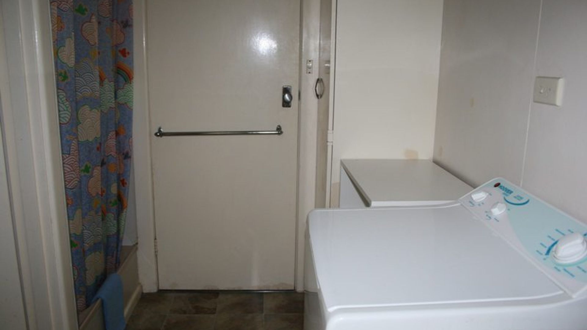 Un lavadero pequeño con lavadora, una puerta con perchero y cortinas estampadas.