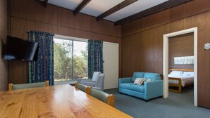 A room with a wooden dining table, a blue sofa, a grey armchair, and a bed with a white headboard. A flat-screen TV is mounted on the wall. - Foreshore Escape Cowes #2 - short walk along the beach to Cowes main street (COWES)