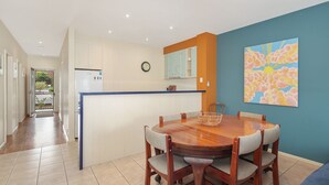 A modern kitchen with a central island, a dining table with chairs, and a large abstract painting on the wall. - The Waves Sanctuary Apartment (COWES)