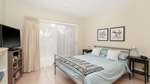 A bedroom with a bed, a TV, a bookshelf, and two framed pictures on the wall. - The Waves Sanctuary Apartment (COWES)