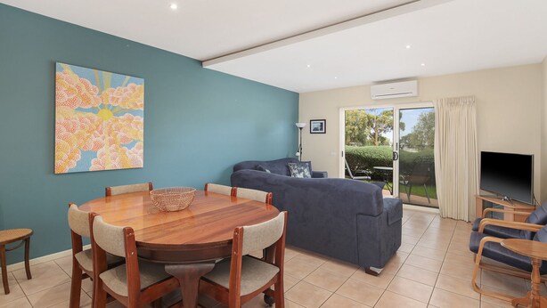A modern living room with a dining table, blue sofa, and a large window overlooking a garden. - The Waves Sanctuary Apartment (COWES)