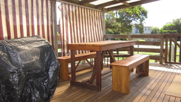 A wooden deck with a picnic table and benches, a covered grill, and a striped awning. - Beachcomber Bliss the perfect family beach house. (SMITHS BEACH)