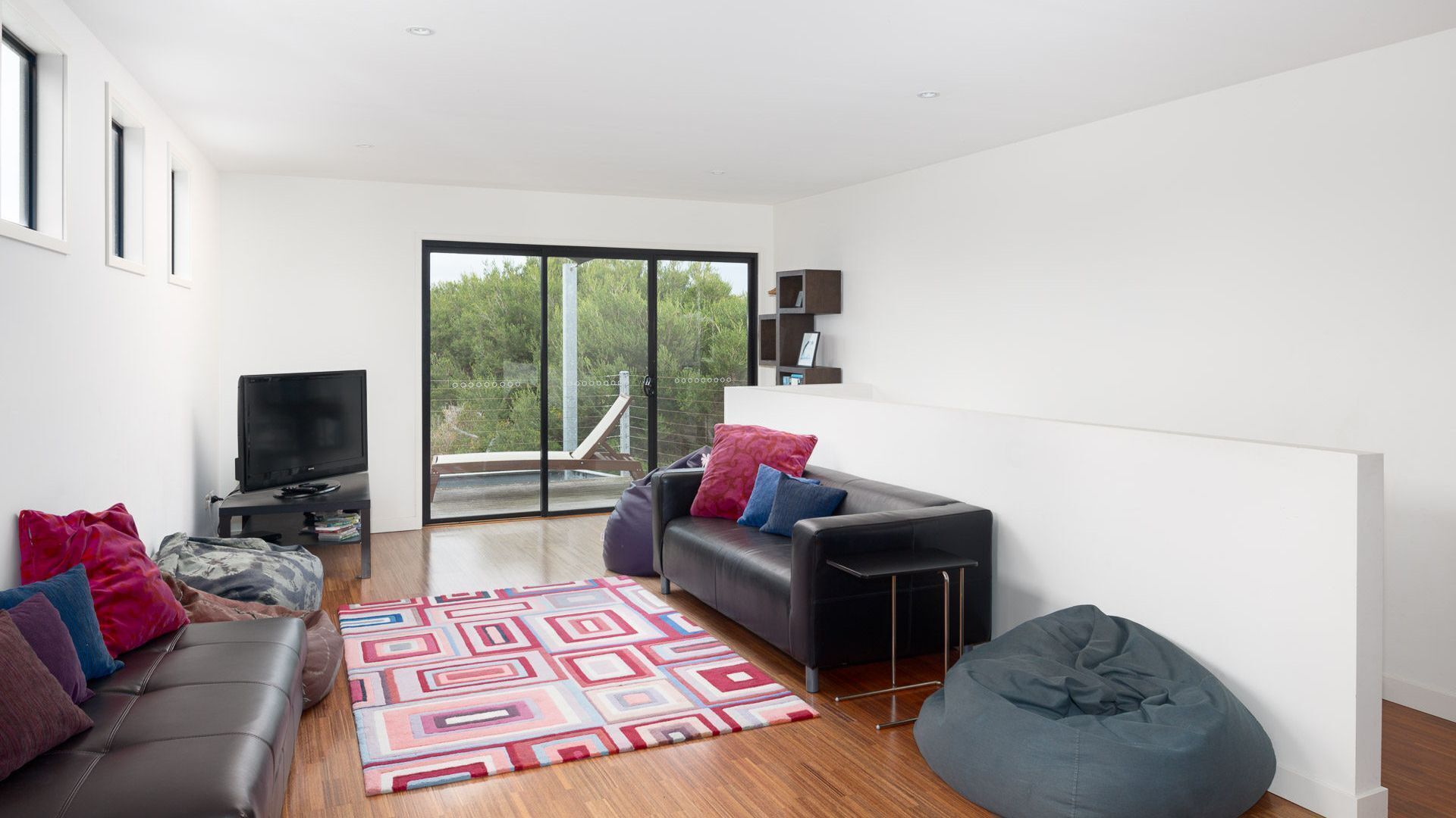 A modern living room with a sofa, a bean bag, a television, and a patterned rug.