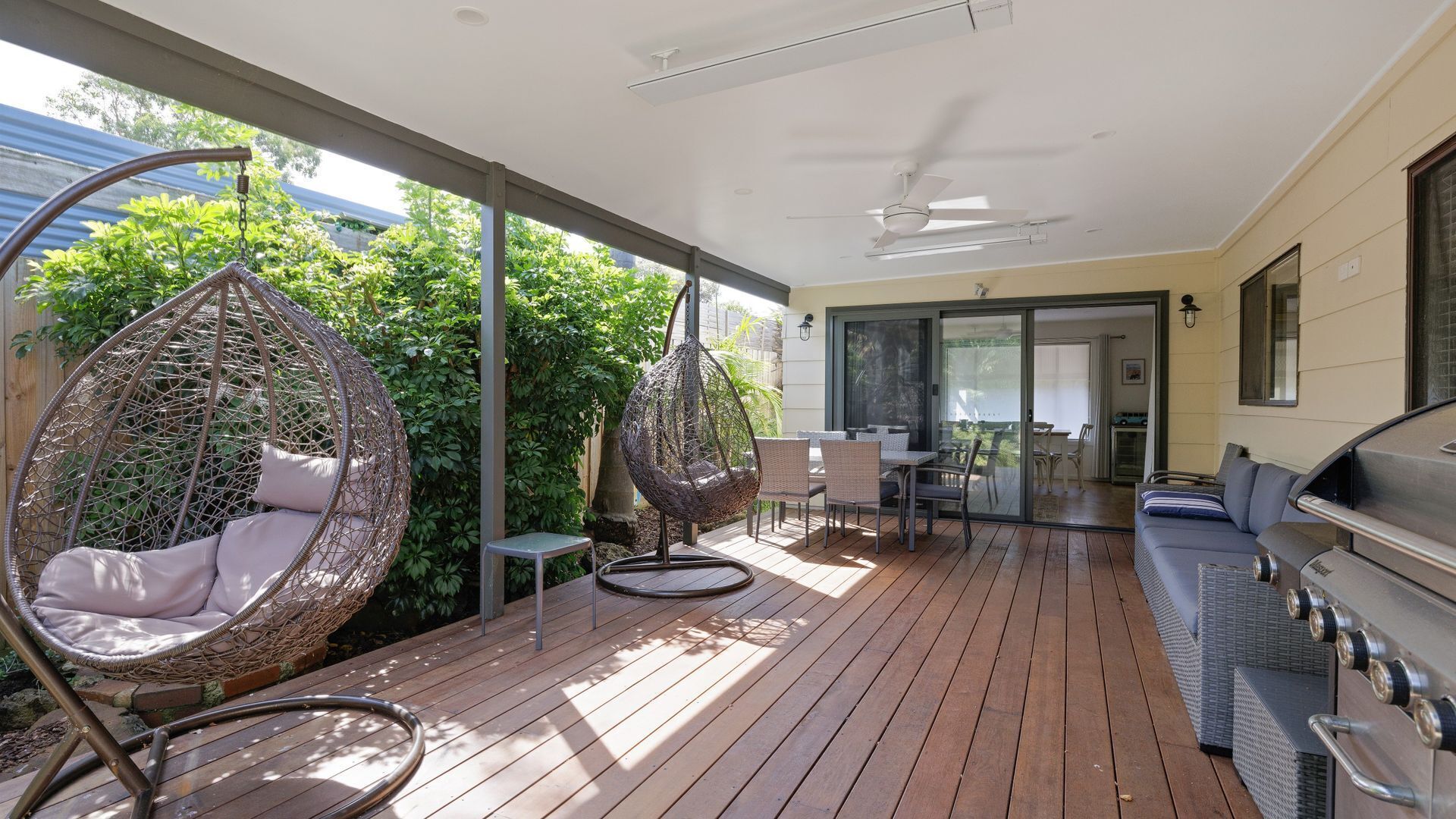 A covered patio with a wooden deck, outdoor furniture, and a barbecue grill.