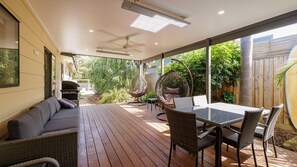 Une terrasse extérieure aménagée avec un canapé, une table à manger, des chaises, un fauteuil suspendu et un ventilateur de plafond.
