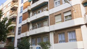 Un immeuble résidentiel à plusieurs étages, doté de balcons, d’un panneau indiquant un espace de stationnement et d’une porte de garage rouge.