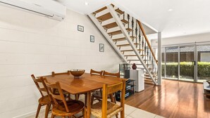 Ein moderner Essbereich mit Holztisch und -stühlen, eine Treppe mit Holzstufen und Metallgeländern sowie ein Blick auf einen Garten durch große Glasüren.