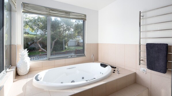 Une salle de bain moderne avec une baignoire sur pieds, une fenêtre donnant sur un espace verdoyant et un porte-serviettes.