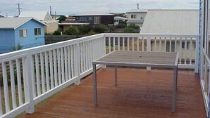 Une terrasse en bois avec une balustrade blanche, une table et des maisons en arrière-plan.