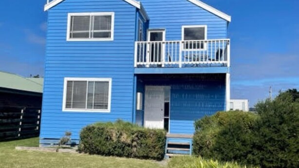 Une maison bleue à deux étages, dotée d’un balcon, d’une porte de garage et d’un petit jardin devant.