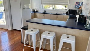Une cuisine dotée d’un îlot central, de tabourets de bar blancs et d’un réfrigérateur.