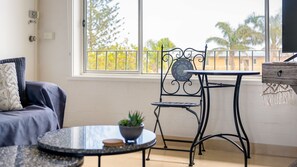 Quarto com sofá, uma mesa redonda com uma planta, uma cadeira de metal e uma pequena mesa de madeira.