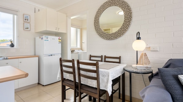 A compact kitchen with white cabinets, a refrigerator, a dining table with chairs, a round mirror, and a small side table with a lamp. - Sea views from centrally located Cowes apartment. (COWES)