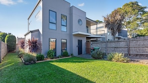 A modern two-story house with a flat roof, a covered patio, and a well-maintained lawn.