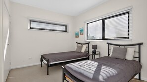 A bedroom with two single beds, a bedside table with a lamp, and a window with blinds.