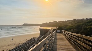 Une promenade en bois menant à une plage, où l’on voit une personne qui se promène.