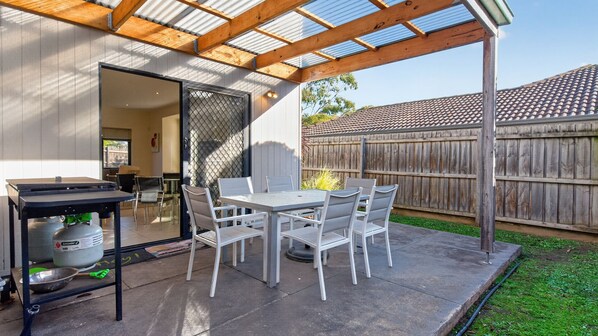 Un patio couvert avec une table et des chaises, une bouteille de gaz et une clôture en bois en arrière-plan.
