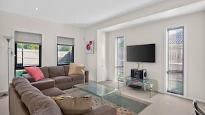 A modern living room with a glass coffee table, a sofa, and a flat-screen TV mounted on the wall.