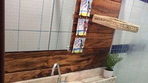 Une salle de bain avec un meuble-lavabo en bois, deux vasques, des toilettes et une étagère suspendue agrémentée d’objets décoratifs.