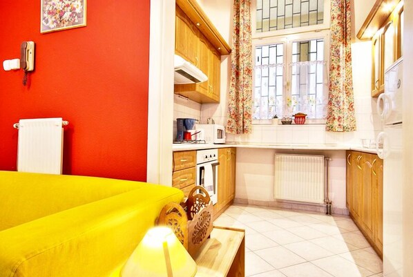 A compact kitchen with wooden cabinets, a microwave, and a window with floral curtains.