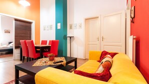 Ein helles Wohnzimmer mit einem gelben Sofa, roten Sesseln und einem Esstisch.