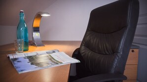 Una mesa de madera con una revista, una botella de vidrio y una lámpara metálica.