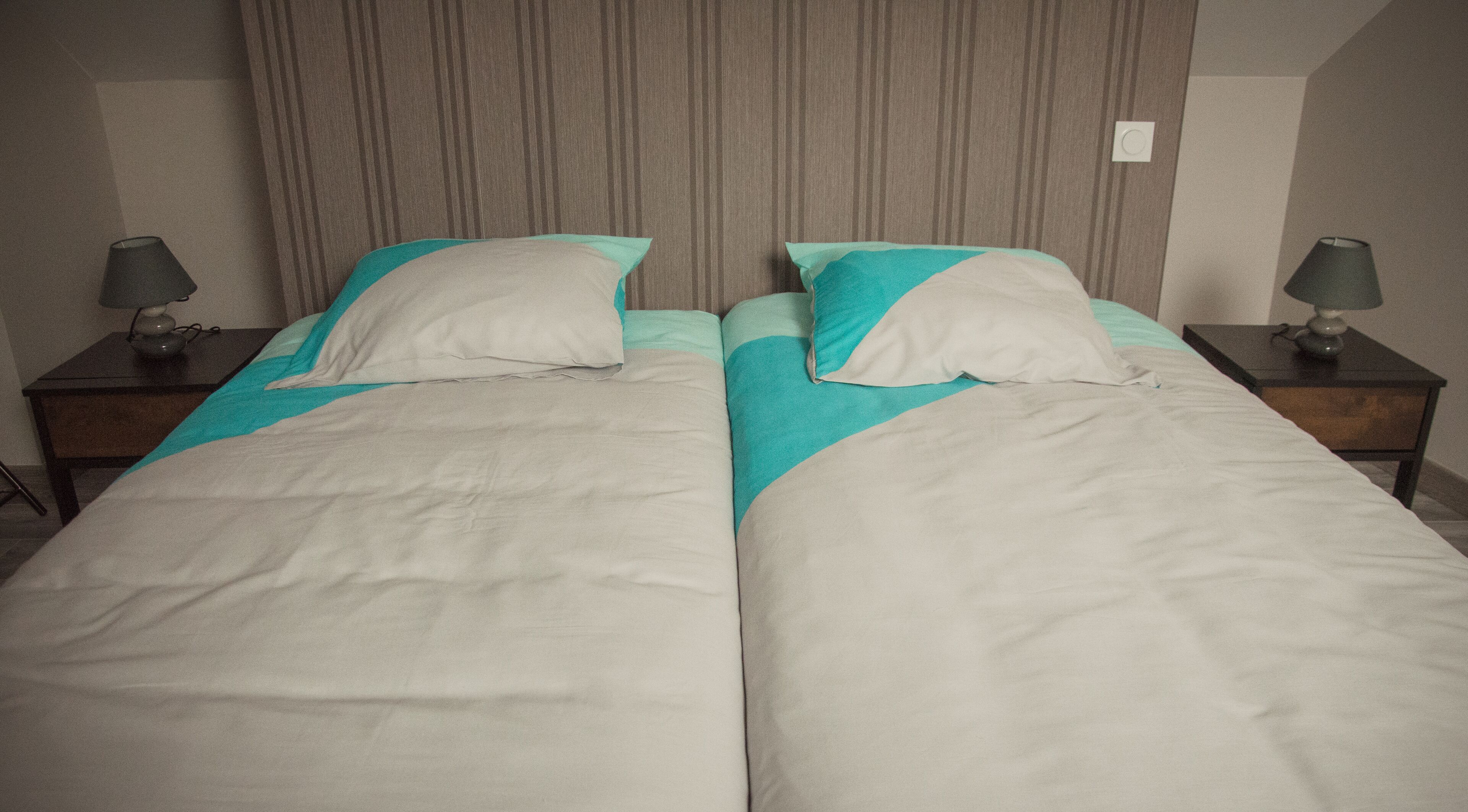 Een tweepersoonsbed met een gestreept hoofdeinde, twee nachtkastjes met lampen en een effen muur.