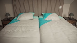 Una cama doble con cabecera a rayas, dos mesitas de noche con lámparas y una pared lisa.