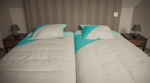 A double bed with a striped headboard, two bedside tables with lamps, and a plain wall.