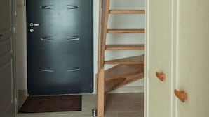 Un pasillo con una puerta oscura, una escalera de madera y un armario blanco.